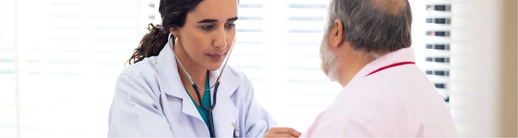 A doctor listens to an older male patient’s chest with a stethoscope in a medical office