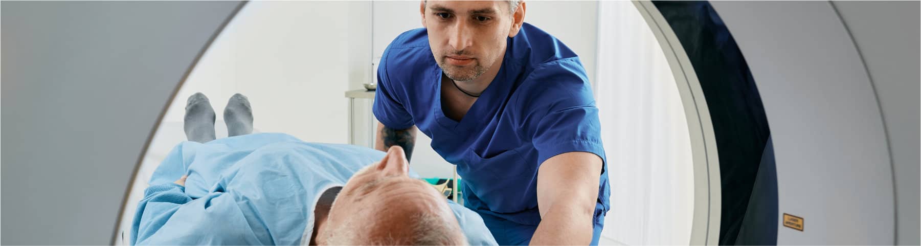 A healthcare worker positions an older patient on a medical imaging scanner