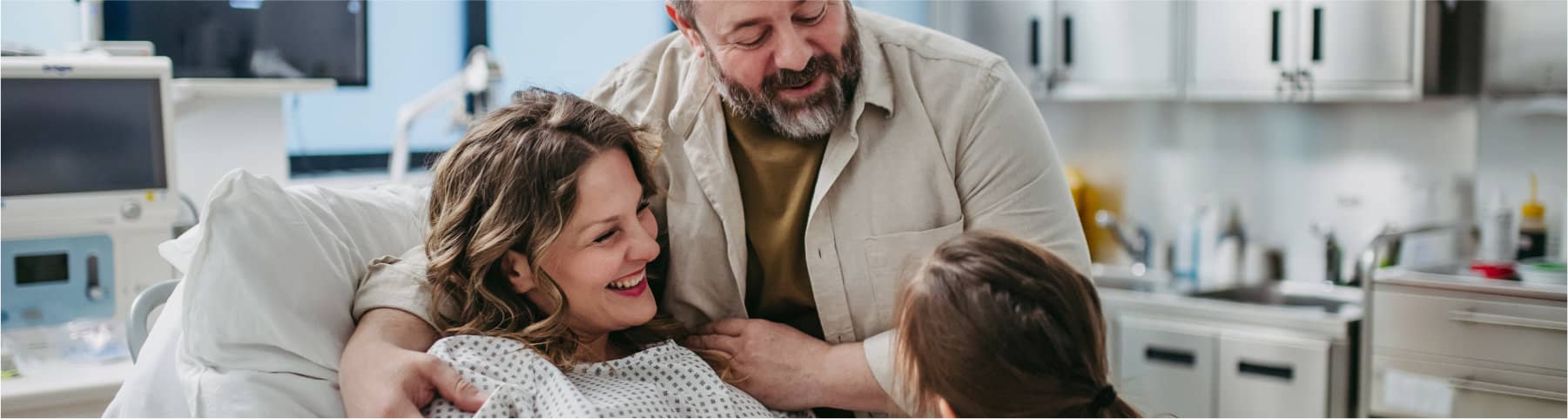 A patient in a hospital bed smiles while being embraced by family members