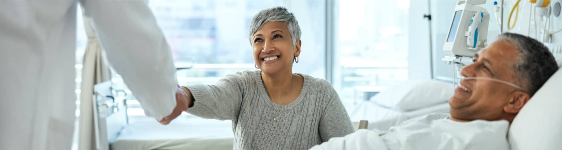 Patient resting in a hospital bed while a loved one speaks with a healthcare provider