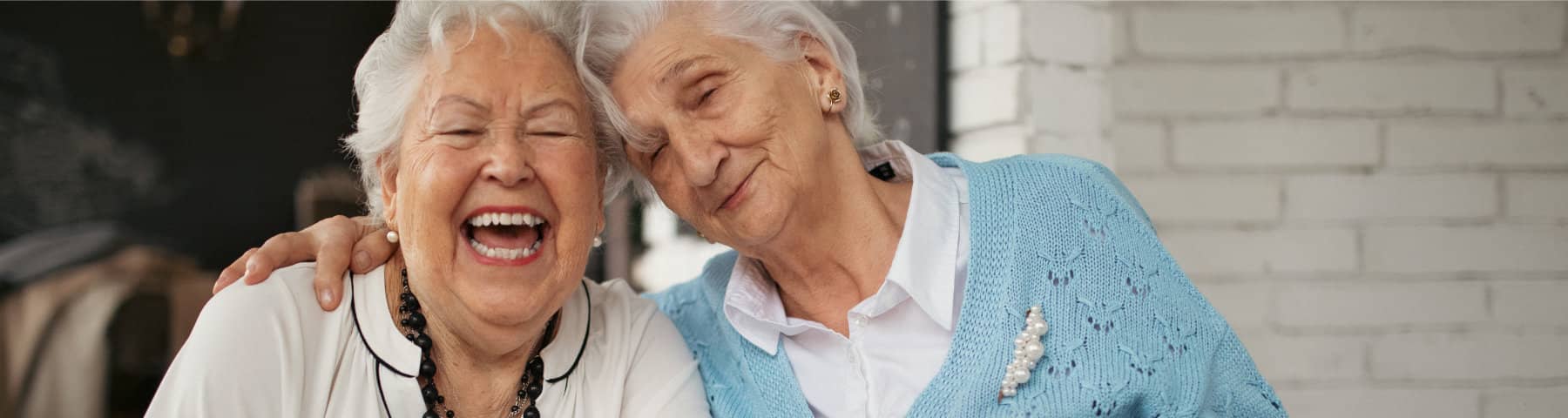 Two older women smiling and embracing in a supportive moment