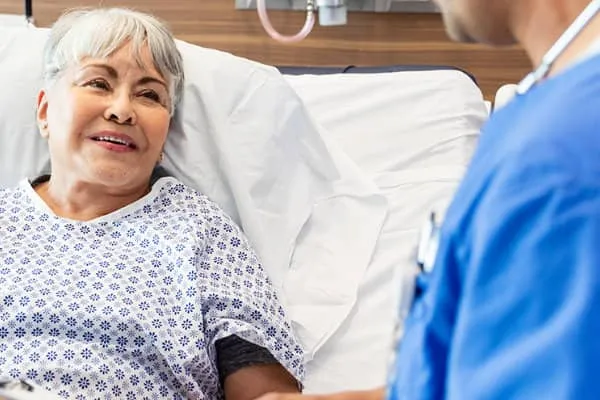 Patient speaking with a healthcare provider while resting in a hospital bed.