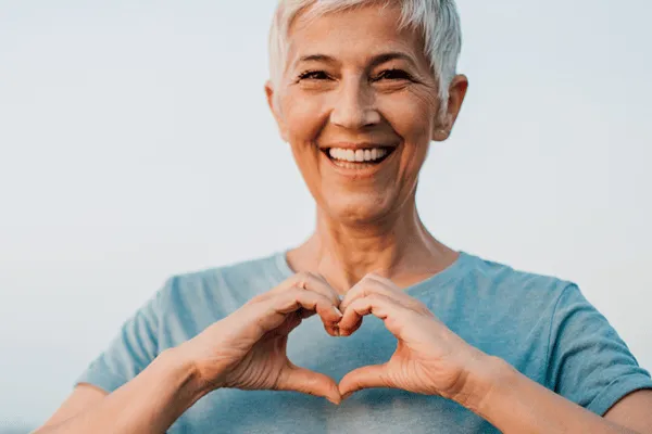 A happy elderly woman forming a heart shape with her hands.