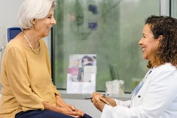 An older woman sitting with a female physician in an examination room, having a heart exam.