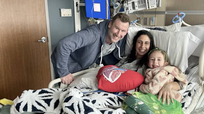 Kristin Fludder with her husband and daughter smiling on a Stony Brook hospital bed